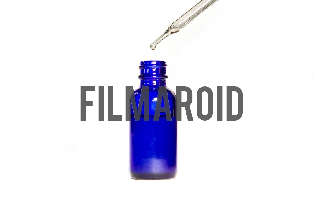 Beautiful cosmetic blue glass bottle without lid and dropper above dripping liquid isolated against white background